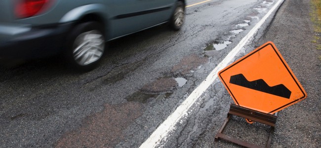 bumps-image Car driving on the road next to potholes with a pothole warning side to the right of them.