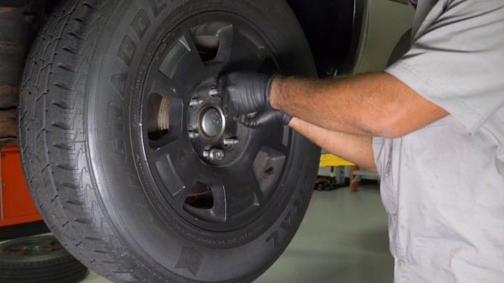 install-struts-chevy-silverado-gmc-sierra-1500-step-13 Technician replacing a wheel on a vehicle which is up on a lift