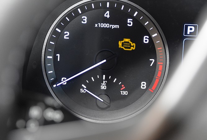 check-engine-light-illuminated-on-dashboard-display A tachometer in a car's dash showing a check engine light illuminated.